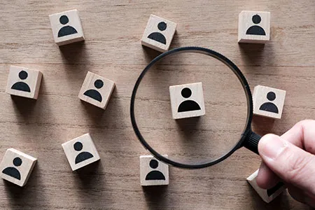 Someone using a magnifying glass to examine wooden block with person icons on them