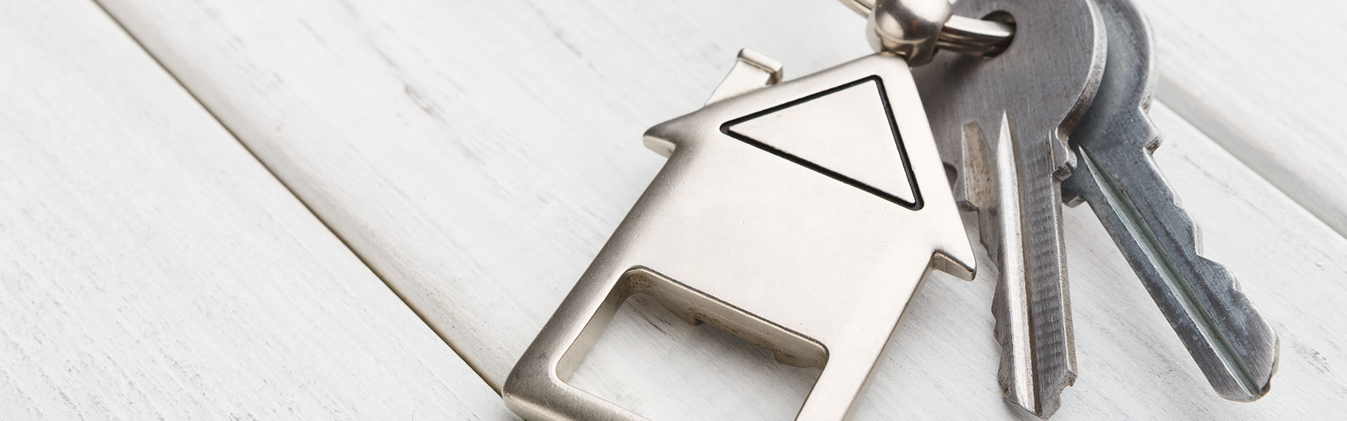 some silver keys with a house keyring on them, sitting on a wooden table